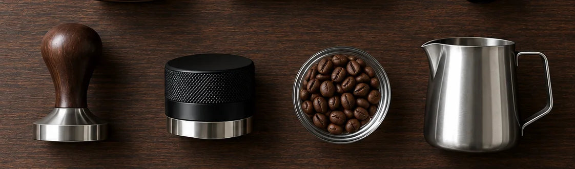 Utensilios de barista sobre madera: tamper, distribuidor, café en grano y jarra para leche